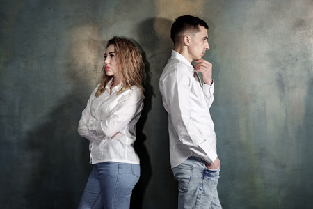 Young couple in love man and woman are offended at each other and no one wants to put up, they are standing with their backs to each other against the wall, tonedの写真素材