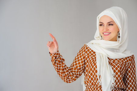Portrait of gorgeous arab woman in headscarf pointing finger at copy space isolated over gray backgroundの写真素材