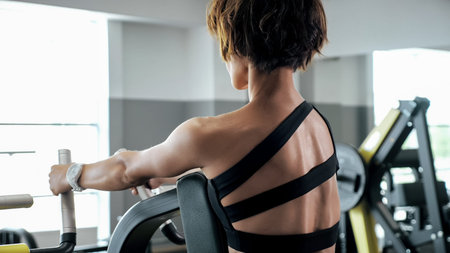Sportive woman is doing exercises for spine muscles on block simulator, back view. Sports workout in...