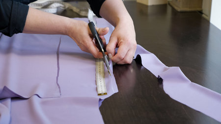 Cutting and sewing products in tailoring business. Tailor woman cutting fabric using large scissors...