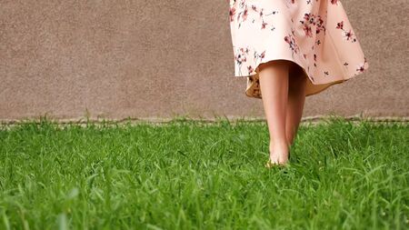 bare feet of slim lady in long pink summer dress walk along lush green grass lawn on warm day close low angle shot copy spaceの写真素材
