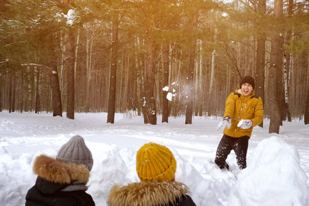 Family is playing snowball fight. Mom and little son are hiding behind snow wall and throwing...