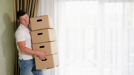 strong man carries large cardboard boxes with belongings to beautiful new house with light and olive...