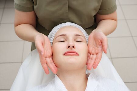 masseuse hands move slowly doing calming face massage to beautiful girl client in medical center view from aboveの写真素材