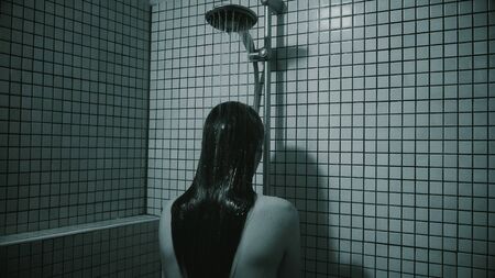 Black and white video of woman with long hairs taking a shower. She is standing by face to wall in bathroom. Depressive mood and solitude state.の写真素材