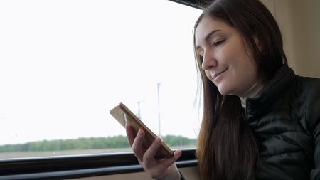 Portrait of young brunette woman traveller is watching something on smartphone. She is riding by...