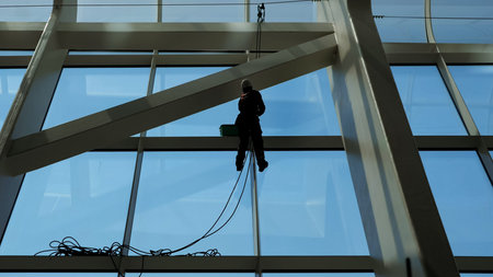 faceless worker man is washing windows with scraper on a highrise modern building hanging the rope.