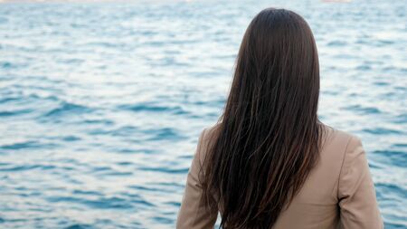 young unrecognizable lady with dark long hair enjoys amazing seascape standing on opposite shore on vacation backside viewの写真素材