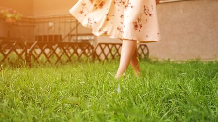 bare feet of slim lady in long pink summer dress walk along lush green grass lawn on warm day close low angle shot copyspaceの写真素材