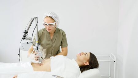 professional therapist makes laser hair removal procedure on attractive lady belly in medical beauty clinicの写真素材
