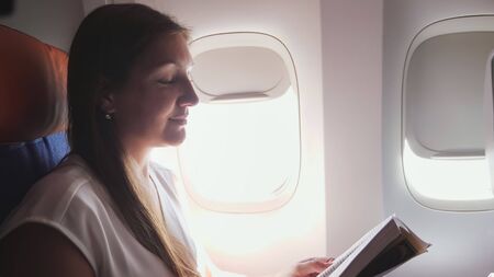 business woman with brown hair wearing grey t-shirt reads book in liner passenger cabin close-upの写真素材