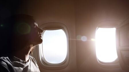 woman in grey t-shirt half-face silhouette against airliner bright windows resting in passenger cabin close viewの写真素材