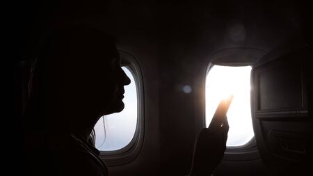 silhouette of girl sits with smartphone against window in airplane closeupの写真素材
