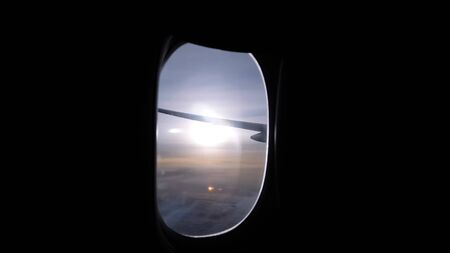 shining bright sun disk over wide horizon under plane wing view from airliner dark passenger cabin portholeの写真素材