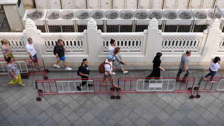 BANGKOK/THAILAND - FEBRUARY 15 2020: Tourists walk along street pavement past traditional fence...