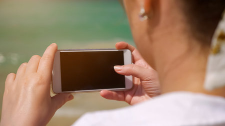 woman in white clothes with silver jewellery in ears takes photos of amazing blurry ocean close...