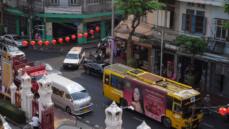 BANGKOK/THAILAND - FEBRUARY 15 2020: Traditional red lanterns over narrow asphalt street road with cars driving in traffic jam among old buildings upper view slow motion on February 15 in Bangkokのeditorial素材