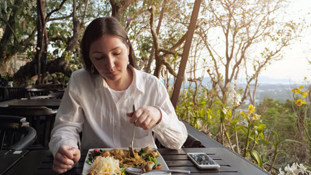 brunette woman has dinner noodles with vegetables in a cafe on the hill.の写真素材