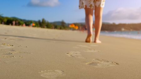 barefoot woman walks on ocean beach wet sand leaving footprints close up sunlightの写真素材