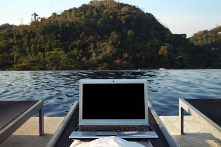 woman with laptop resting alone in lounge chair at hotel pool against forestry hill close back viewの写真素材