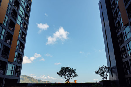 white clouds float on boundless blue sky between modern highrise buildings with windows reflecting...
