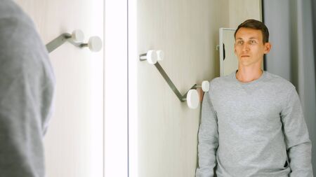 Handsome man in a gray sweatshirt in front of a fitting room mirror.の写真素材