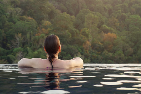 Young woman relaxing in the swimming pool backside view