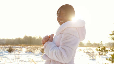 African-American lady in white fur coat in snowy field at back sunlight close upの写真素材
