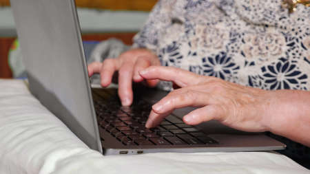 Close-up of hands of an elderly woman typing on a laptop.の写真素材