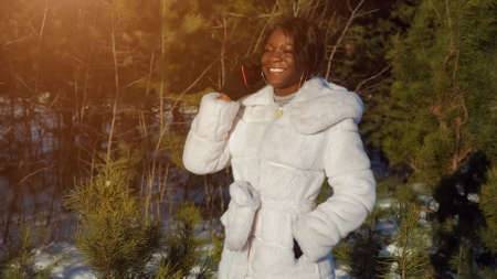 black woman in earrings talks on digital gadget with friends standing against evergreen pines in forest closeupの写真素材
