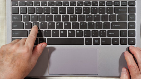 Close up of keyboard and hands of an elderly woman typing on a laptop top viewの写真素材