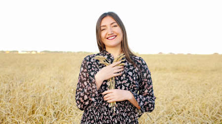 Young woman with a bouquet of ears of ripe wheat in the field.の写真素材