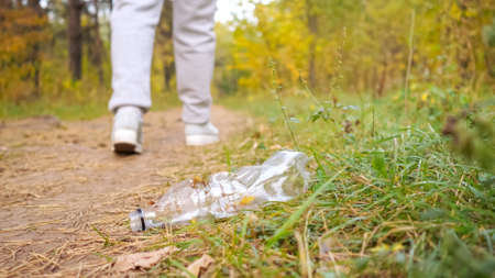 Unrecognizable woman throws a plastic bottle into the grass in the forest.の写真素材