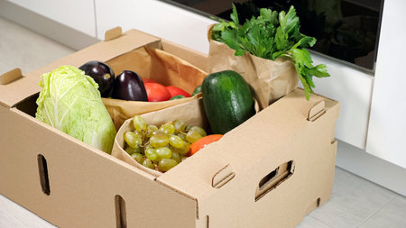 man puts brown cardboard container with various vegetables on floor at kitchen close-up