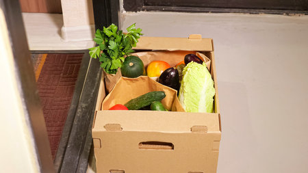 Delivery guy puts large brown cardboard box with ordered fresh vegetables on white floor and black...