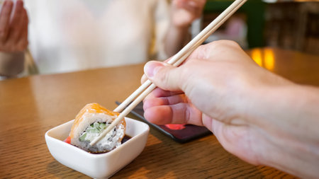 Male hand dipping roll with chopsticks in soy sauce.の写真素材