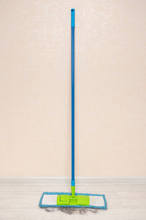 blue mop stands against a wall with collected trash on the floor.