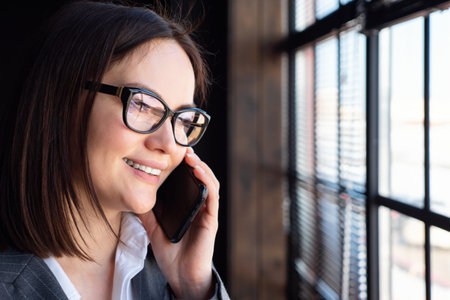 Close-up of young woman talking on the phone by the window.の写真素材
