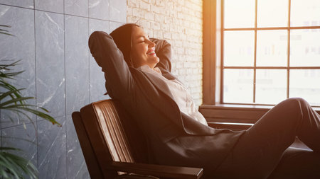 Delighted businesswoman with short dark hair sits down falling on brown bench with happy smile in...