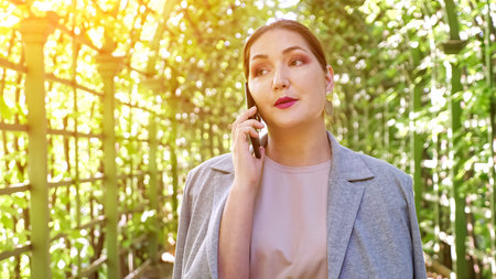 Close-up woman talking on the phone in a garden arch, sunlight