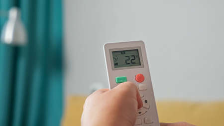 Close-up of a hand regulating an air conditioner with a remote control.の写真素材