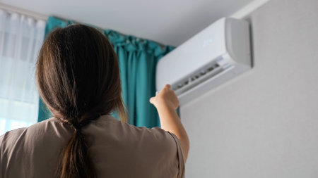 Unrecognizable woman turns on the air conditioner, back view.の写真素材
