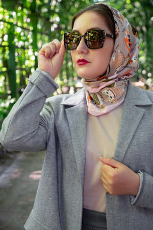 Portrait of stylish muslim lady in grey suit and sunglasses poses at park, fashion style trend.の写真素材