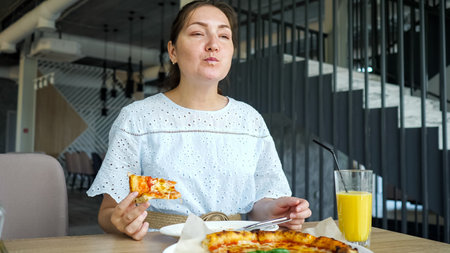 pretty brunette woman in blue dress eats pizza in restaurant, side view
