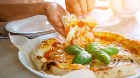 Lady eats pizza. Young woman hands take delicious snack slice and put on white plate near tea cup on...