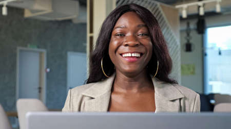 Concentrated African-American businesswoman gets good news and becomes excited working on modern laptop in cozy restaurant close viewの写真素材