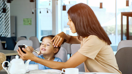 Mother helps girl apply make-up. Asian woman brunette holds small mirror and toddler daughter moves...