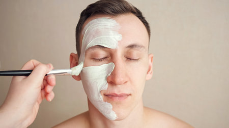 Beautician applies a mask to a handsome man with brush on face.
