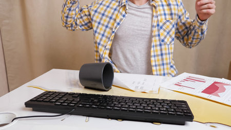 Unrecognizable man works with documents and types text on the keyboard, throws coffee on the table.
