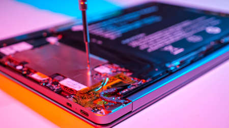 Unrecognizable man disassembles laptop with screwdriver in muted red and blue light closeupの写真素材